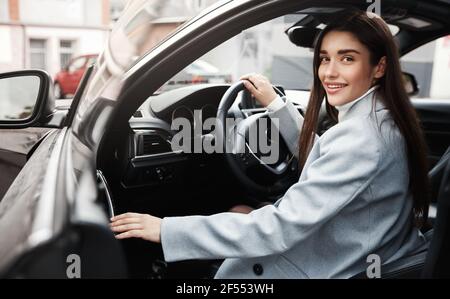 Successful businesswoman getting out of car and smiling. Female executive getting in vehicle to drive at work Stock Photo