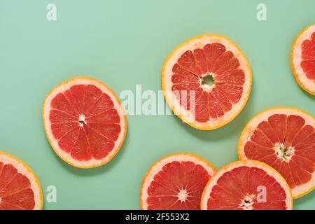 Grapefruit citrus pattern composition. Grapefruit slices with juice are scattered around on a green background with shadows. Summer or spring concept. Stock Photo