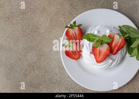 Mini Pavlova meringue cakes with strawberries and mint on a plate, concrete background. Selective focus. Stock Photo