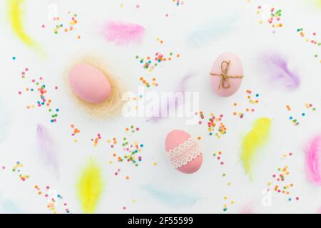 Ester composition with colorful eggs, feathers and confetti on white background. Flat lay, top view Stock Photo