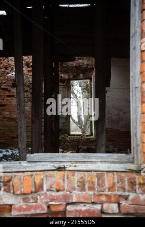 abandoned collapsed red brick building interior through an old wooden window frame. the view takes you to the opposite window, through which you can s