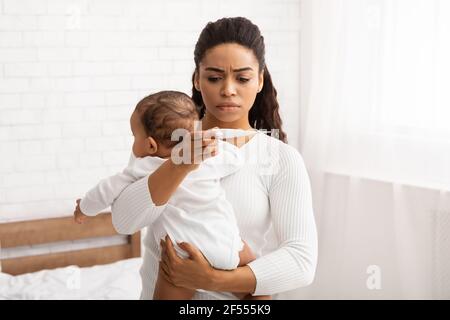Mother Caring For Sick Baby With Fever Holding Thermometer Indoor Stock Photo