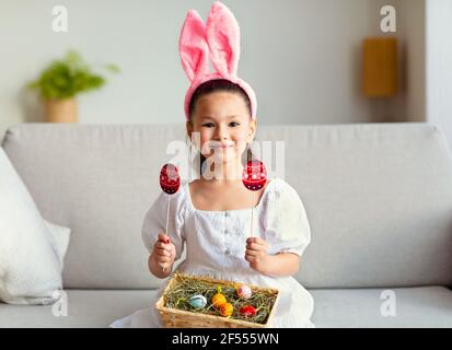 Girl Wearing Easter Bunny Ears Holding Basket With Eggs Indoors Stock Photo