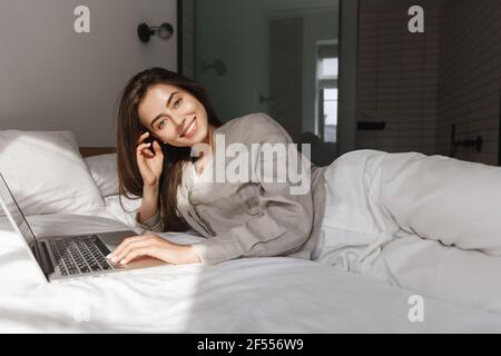 Woman lying on bed and working with laptop at home. Girl resting in bedroom with computer Stock Photo