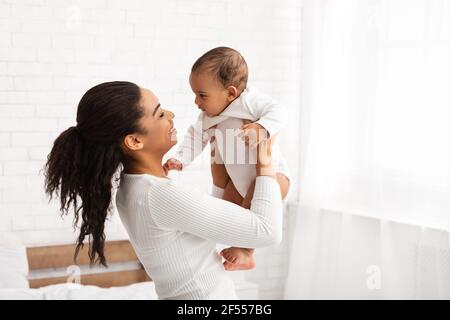 Joyful African Mother Carrying Baby Playing With Newborn At Home Stock Photo