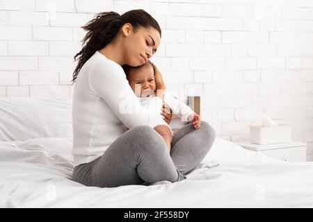 African Mother Hushing Crying Newborn Baby To Sleep In Bedroom Stock Photo