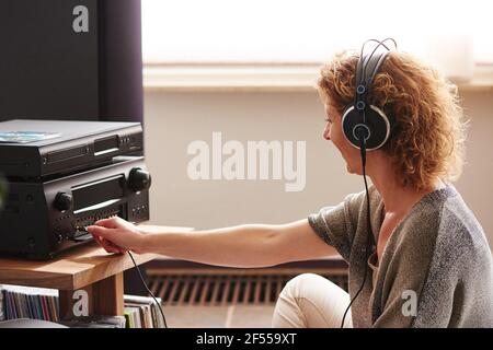 Side portrait of woman pressing button on sound system wearing headphones Stock Photo