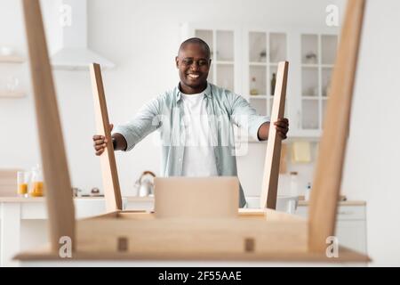 Assemble new furniture at home by yourself. Happy african american man installing wooden desk after home relocation Stock Photo