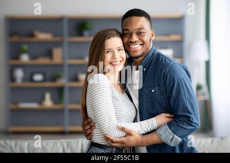 Portrait Of Romantic Interracial Couple Embracing And Smiling At Camera Stock Photo