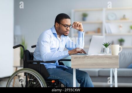 Focused young man in wheelchair using laptop computer for online work or communication at home Stock Photo