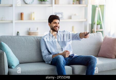 Watching TV. Happy arab man having rest, switching channels with remote controller Stock Photo