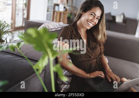 Amused happy good-looking hispanic young female employee sit office lounge zone couch holding laptop laughing camera joyfully smiling relaxing Stock Photo