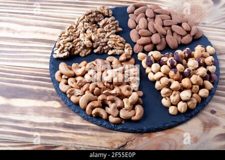 Various nuts sorted in glass bowl with honey bowl and honey dipper. Mixed nuts on wooden table. Black stone plate on wooden background. Stock Photo