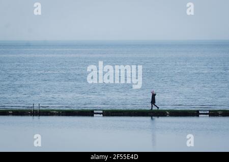 A woman walks on the wall of the boating pond at the seafront in Margate, Kent. Picture date: Wednesday March 24, 2021. Stock Photo