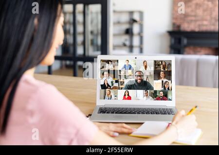Back view over shoulder of a woman on a laptop screen with a diverse team, video conference with employees, brainstorm, online video meeting with coworkers Stock Photo