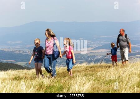 Family with children on a trip, active grandparents, girls, kids holding hands and walking in the meadow Stock Photo