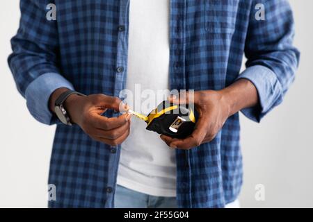 Home repairman. Unrecognizable black man holding measuring tape over white studio background, studio shot, closeup Stock Photo