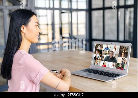 An Asian woman and diverse team on the laptop screen are talking and discussion via video connection, have online meeting, remote conference. Remote work concept Stock Photo