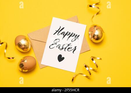 Happy Easter composition with blank paper and greeting text, gold eggs and serpentine on bright yellow background Stock Photo