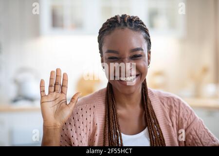 Closeup of cheerful black lady waving hand at camera, making video call