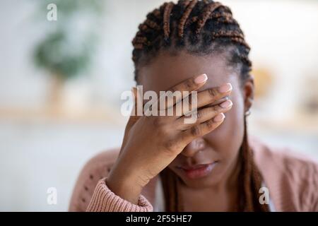 Closeup portrait of depressed young black woman touching head in despair Stock Photo