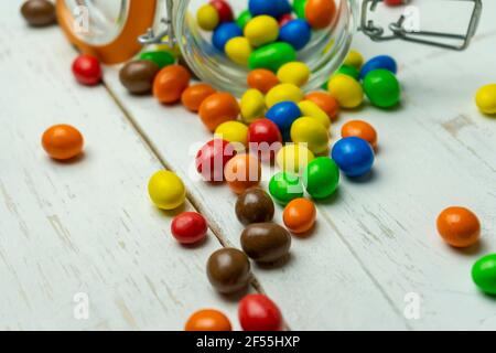 Creative colorful candies background.Confectionery scattered multicolored chocolate sweets on white wooden background. Stock Photo
