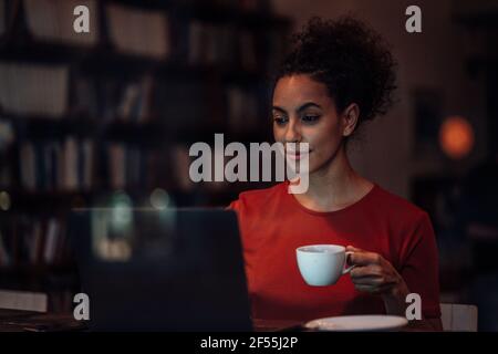 Young woman having coffee while working on laptop sitting at cafe Stock Photo