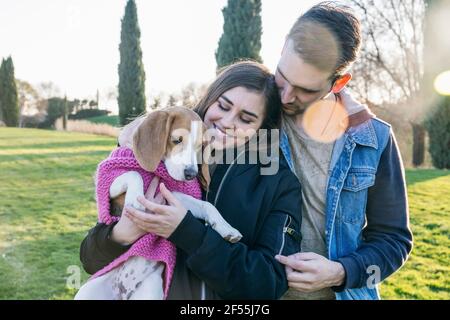 Pet owners looking at dog in sweater while standing at park Stock Photo