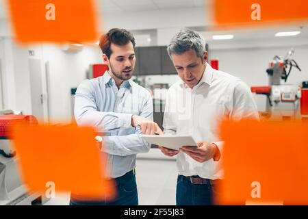 Male engineers seen through glass wall while discussing about business plans in factory Stock Photo
