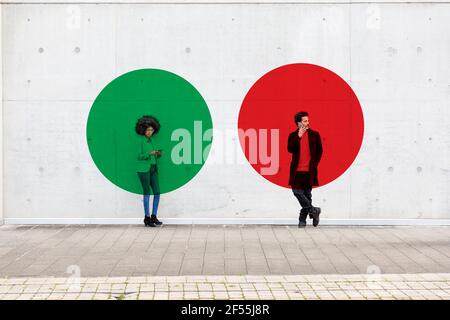 Two circles visualizing social distancing covering man and woman standing outdoors with smart phones in hands Stock Photo
