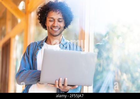 Smiling man using laptop while standing by front yard window Stock Photo