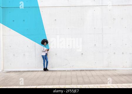 Young woman standing outdoors with smart phone in hands covered in blue facial recognition effect Stock Photo