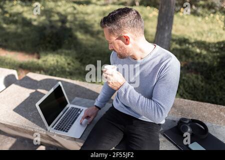 Male entrepreneur with disposable coffee cup using laptop Stock Photo