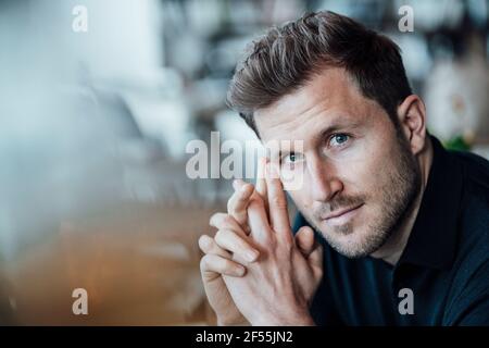 Businessman with hands clasped staring while sitting at cafe