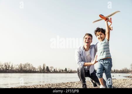 Playful boy playing with airplane toy by father crouching on pebbles Stock Photo