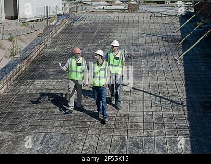Three male construction workers walking and talking at construction site Stock Photo