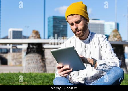 Handsome man using digital tablet while sitting at park during sunny day Stock Photo