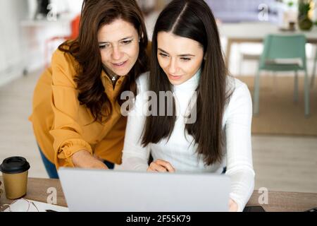 Mother assisting daughter while studying on laptop at home Stock Photo