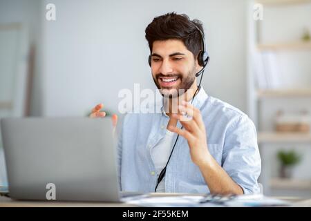 Positive arab male teacher having virtual lesson via video call, explaining lecture remotely using laptop Stock Photo