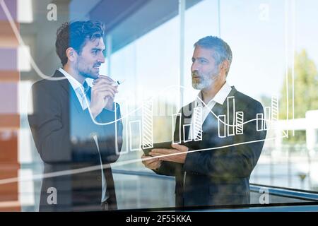 Businessmen discussing over graph while standing in modern office Stock Photo