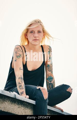 Tattooed young woman sitting on rooftop Stock Photo