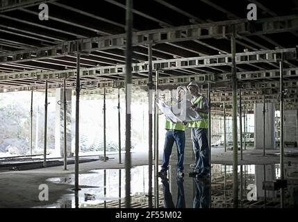 Two male construction workers talking over plans at construction site Stock Photo