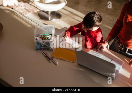 Mother assisting son while studying at dining table at home Stock Photo