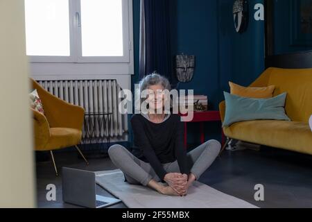 Smiling senior woman practicing Yoga on exercise mat at home Stock Photo