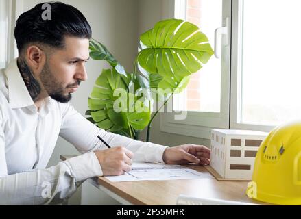 Male architect looking at architectural model while drawing blueprint in office Stock Photo