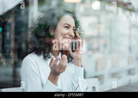 Young businesswoman smiling while talking on mobile phone sitting at cafe Stock Photo