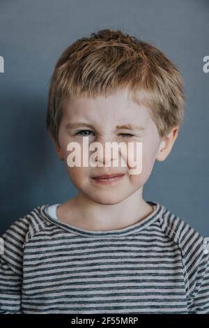 Playful boy winking against gray background Stock Photo