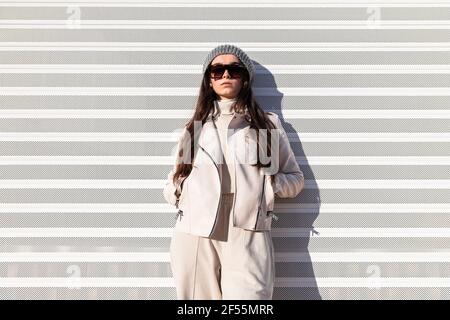 Fashionable teenage girl with hands in pockets standing while leaning on white wall Stock Photo