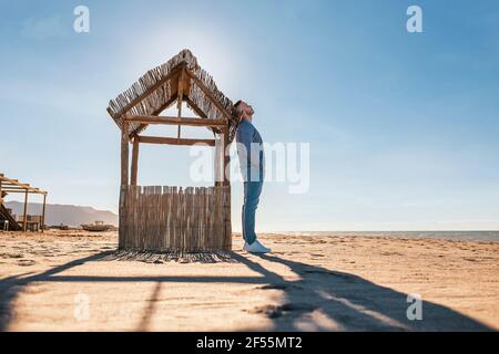 Mid adult man with hands in pockets relaxing while leaning on wooden stall Stock Photo