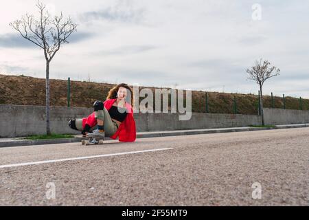 Smiling female skater with skateboard sitting on road against sky Stock Photo